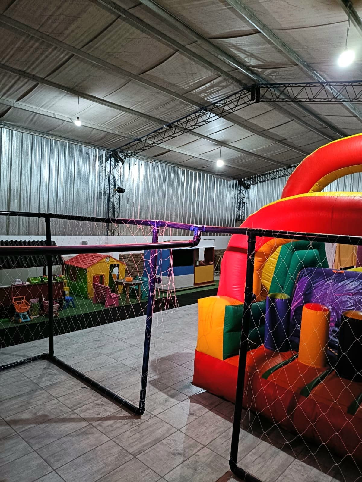 Parque infantil interior con un gran inflable multicolor, casita de juegos y redes de seguridad.