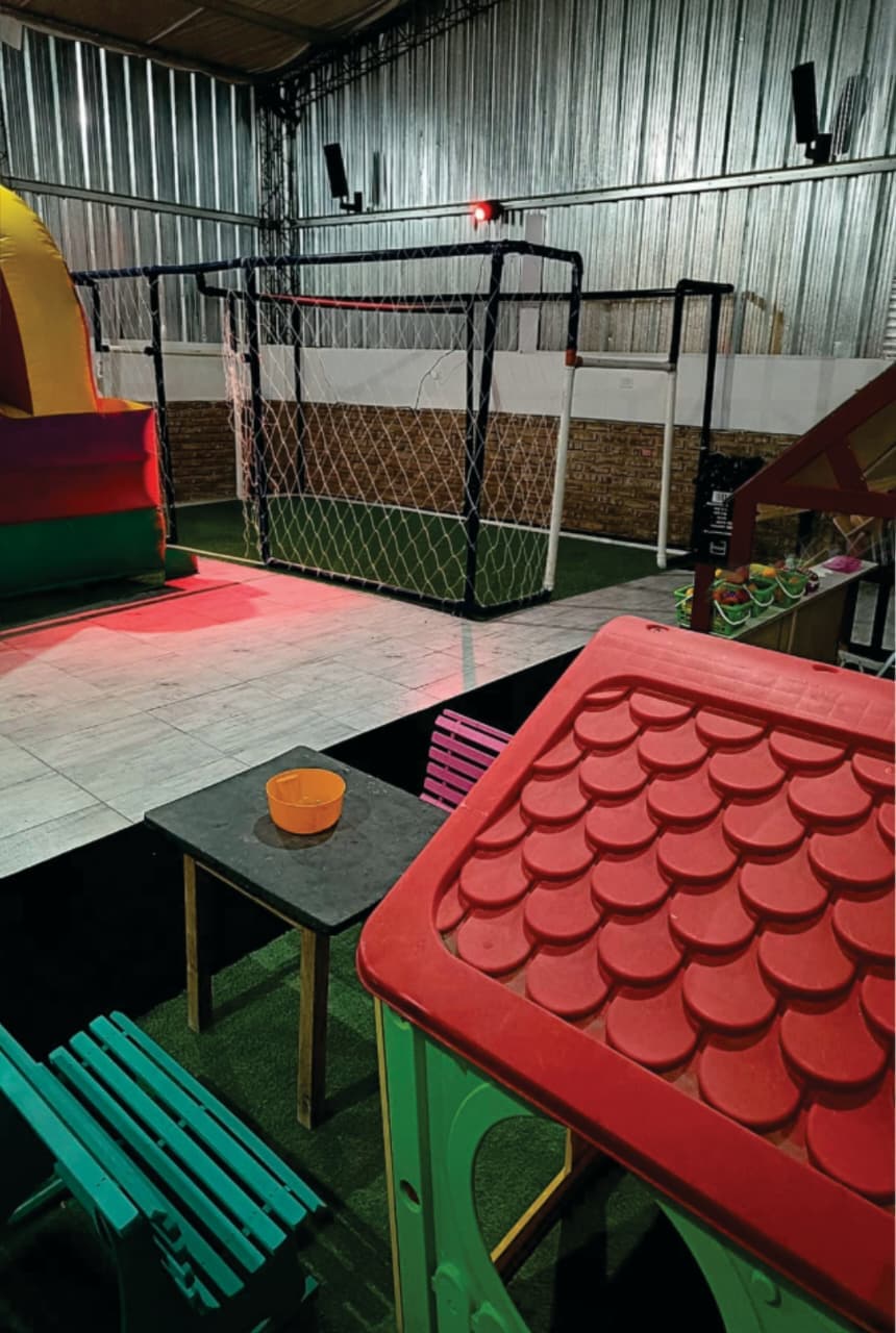 Área de juegos interior con casita roja, portería de fútbol y un inflable colorido.