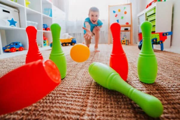 Niño lanza una bola amarilla a bolos de plástico de colores en su habitación.